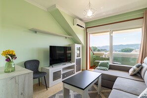 Un salón con televisor, sofá y balcón con vistas.