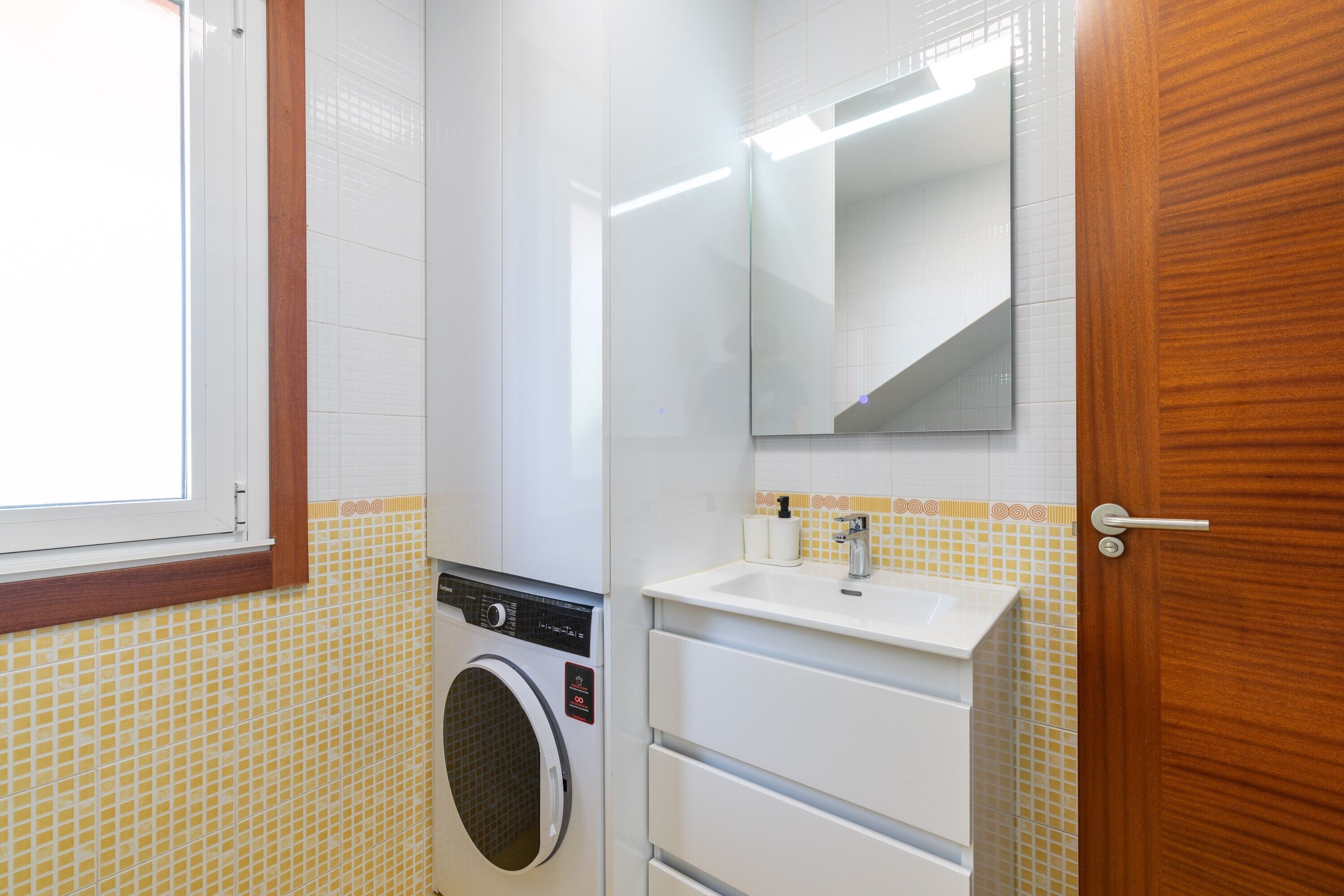 Un baño con lavadora, lavamanos y espejo.