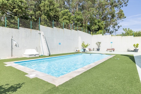A swimming pool with a concrete border, surrounded by artificial grass, a white lounge chair, and a bench.. Penthouse in Palmeira with Sea Views, Shared Pool, Tennis Court and Wi-Fi