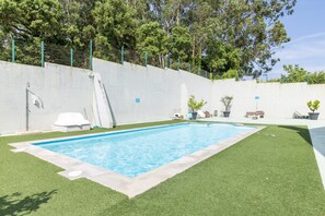Piscina com borda de concreto, rodeada por grama sintética, uma cadeira de lounge branca e um banco.