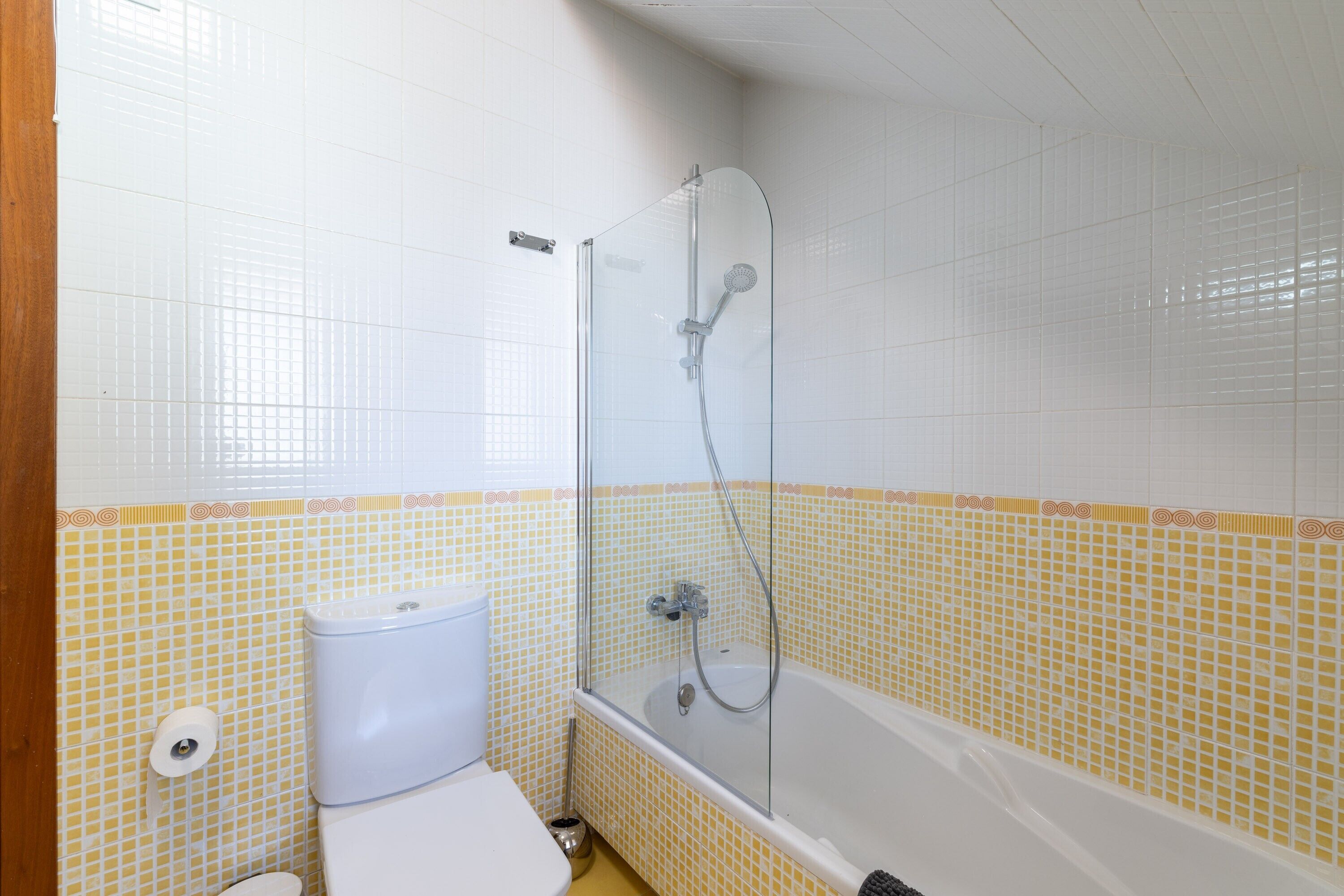 Un baño con ducha, inodoro y pared de azulejos.