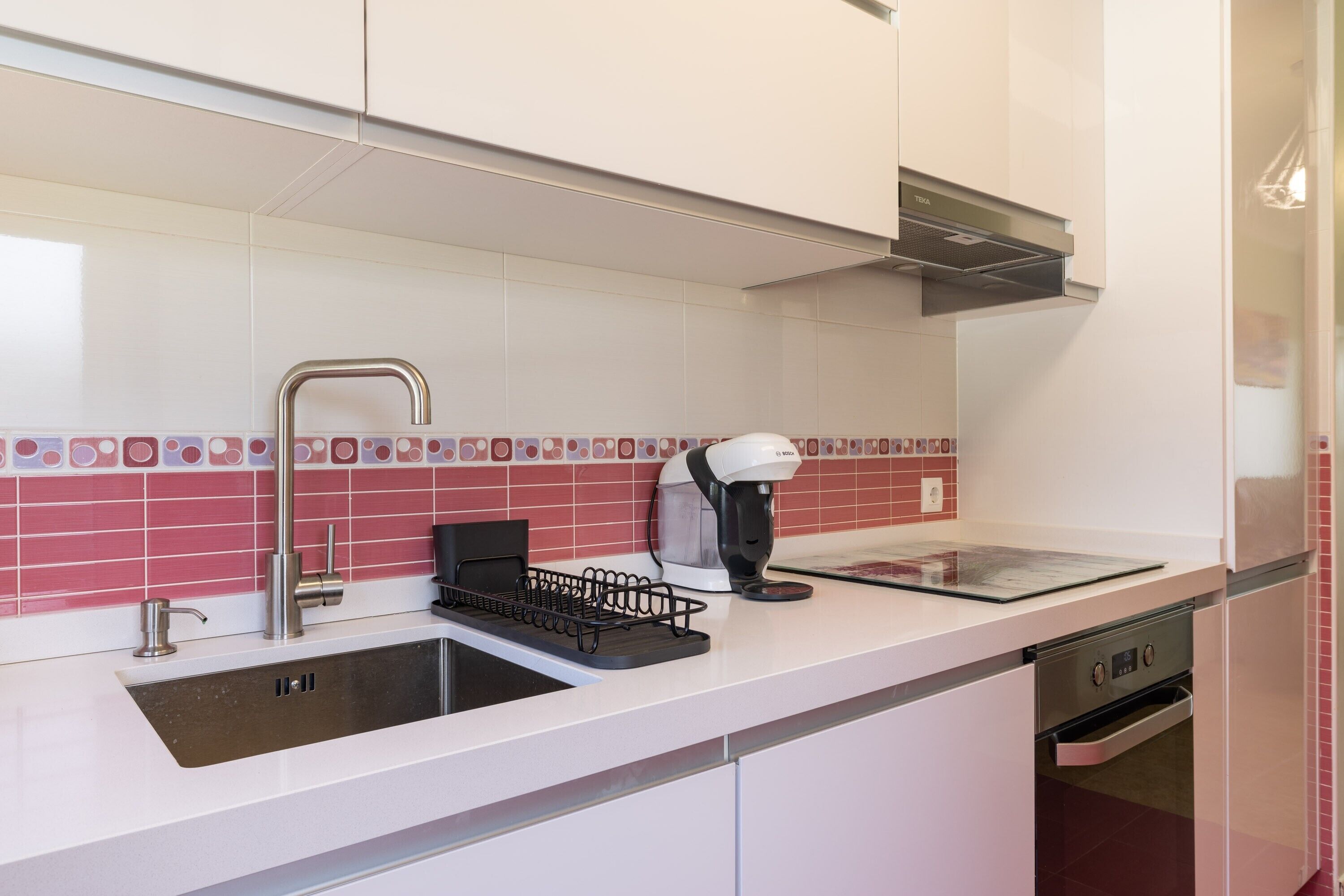 Una cocina moderna con un lavamanos de acero inoxidable, una cafetera y un horno empotrado.