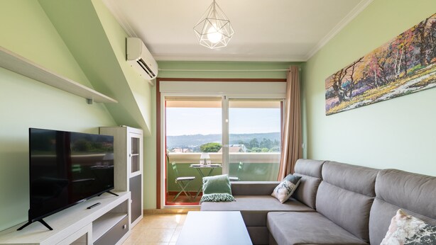 A living room with a flat-screen TV, a sofa, a coffee table, and a balcony with a table and chairs. - Penthouse in Palmeira with Sea Views, Shared Pool, Tennis Court and Wi-Fi (Insuela)