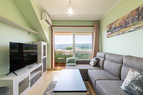 A living room with a flat-screen TV, a sofa, a coffee table, and a balcony with a table and chairs.. Penthouse in Palmeira with Sea Views, Shared Pool, Tennis Court and Wi-Fi