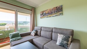 A living room with a sofa, a painting, and a view of the outdoors. - Penthouse in Palmeira with Sea Views, Shared Pool, Tennis Court and Wi-Fi (Insuela)
