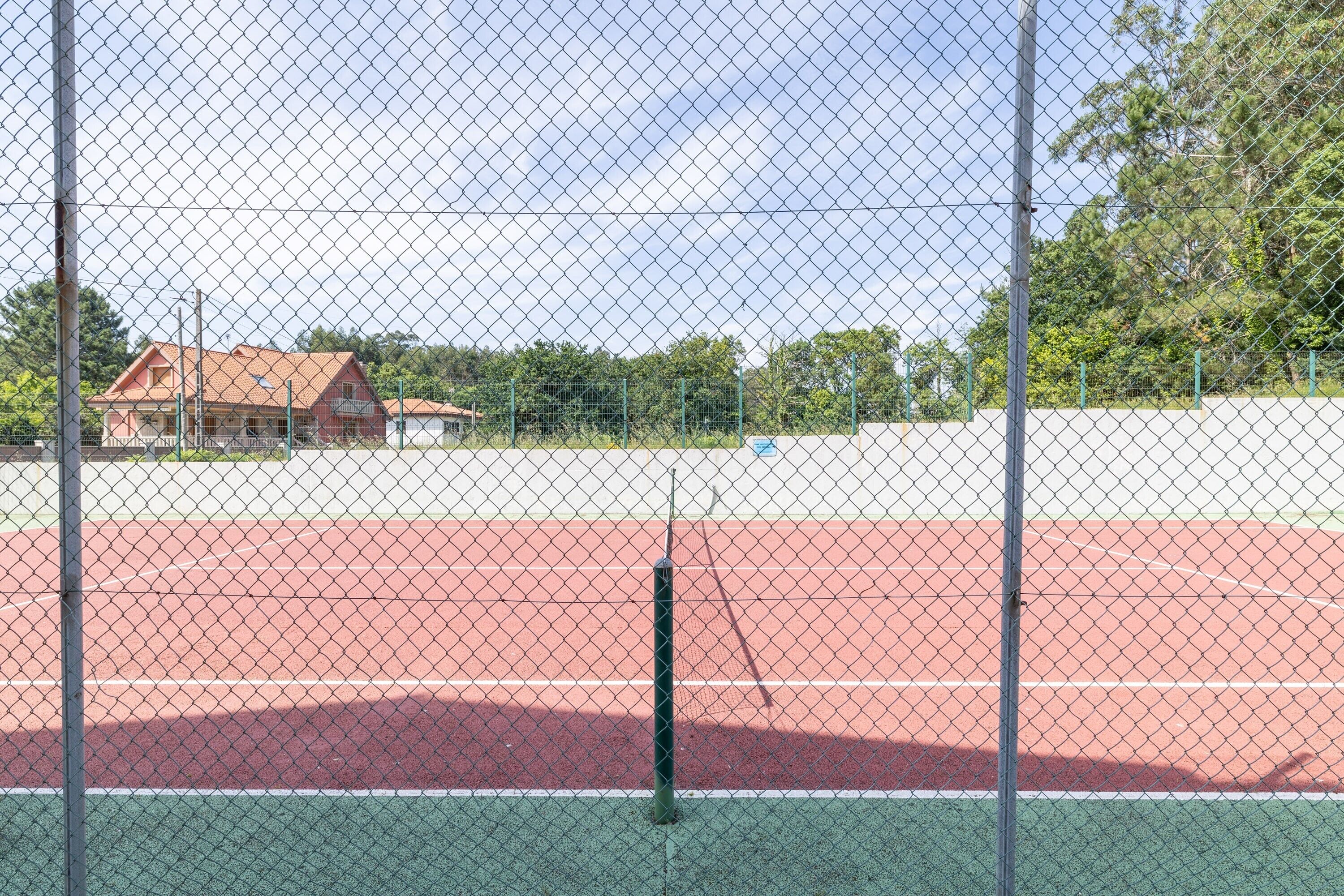 A tennis court enclosed by a chain-link fence with a house in the background.