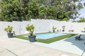 Una piscina con césped artificial, plantas en macetas y un banco.