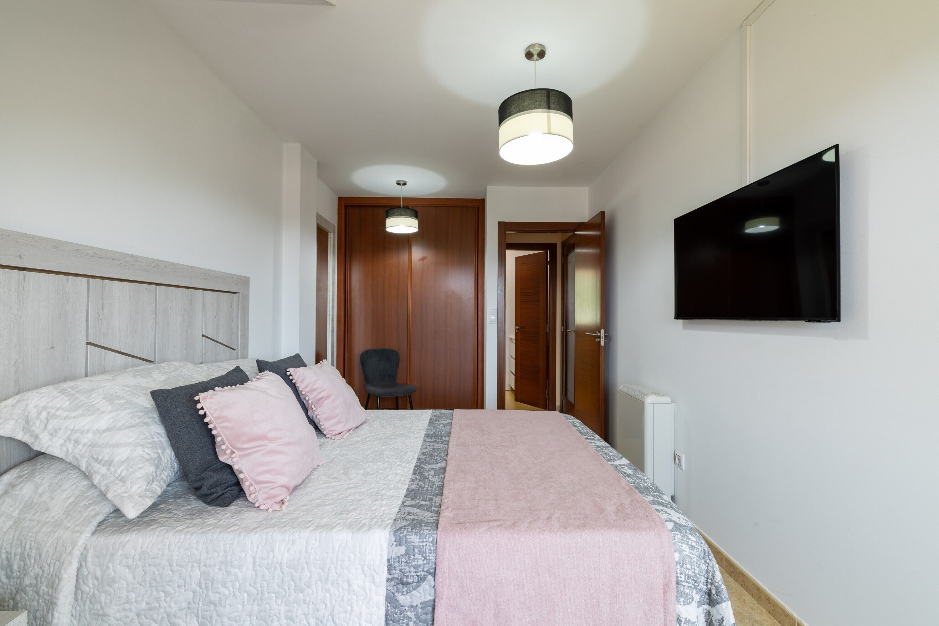 A bedroom with a bed, pillows, a TV, and a chair.