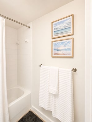 A bathroom with a bathtub, a shower curtain, and two framed pictures on the wall.