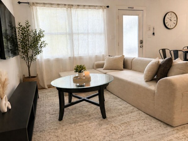 Ein Wohnzimmer mit einer Couch, einem runden Couchtisch, einer Zimmerpflanze und einer Wanduhr.