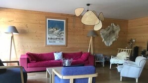Una habitación con pared de madera, un sofá rojo, un sillón azul, una silla blanca y un ventilador de techo.