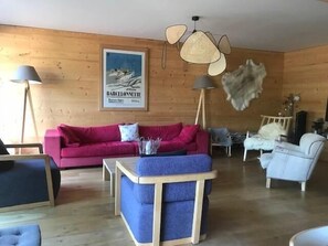 Ein Zimmer mit einer Holzwand, einem roten Sofa, einem blauen Sessel, einem weißen Stuhl und einem Deckenventilator.