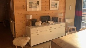 Una habitación con paneles de madera, un tocador blanco, dos cuadros en la pared, una silla y un perro blanco pequeño.