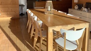 Una cocina moderna con paredes de madera, una isla central, sillas blancas y lámparas colgantes, con vista al área de comedor.