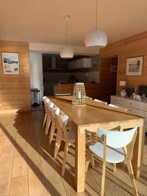 Eine moderne Küche mit Holzwänden, einer zentralen Kochinsel, weißen Stühlen, Pendelleuchten und Blick in den Essbereich.
