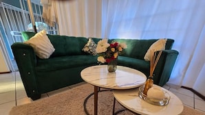 A green sofa with a vase of flowers and a pair of glasses on a round table. - Room-aquasaints Guest Lodge (Johannesburg)