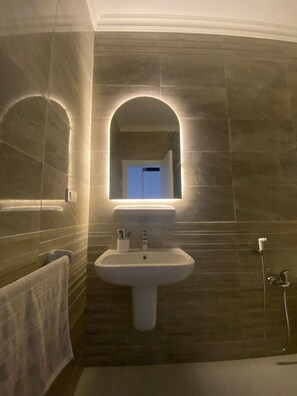 A bathroom with a pedestal sink, a mirror with an arch, and a towel rack.