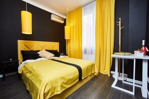 Ett hotellrum med en säng, ett nattduksbord, ett bord med en flaska och ett bricka, och ett fönster med gula gardiner.