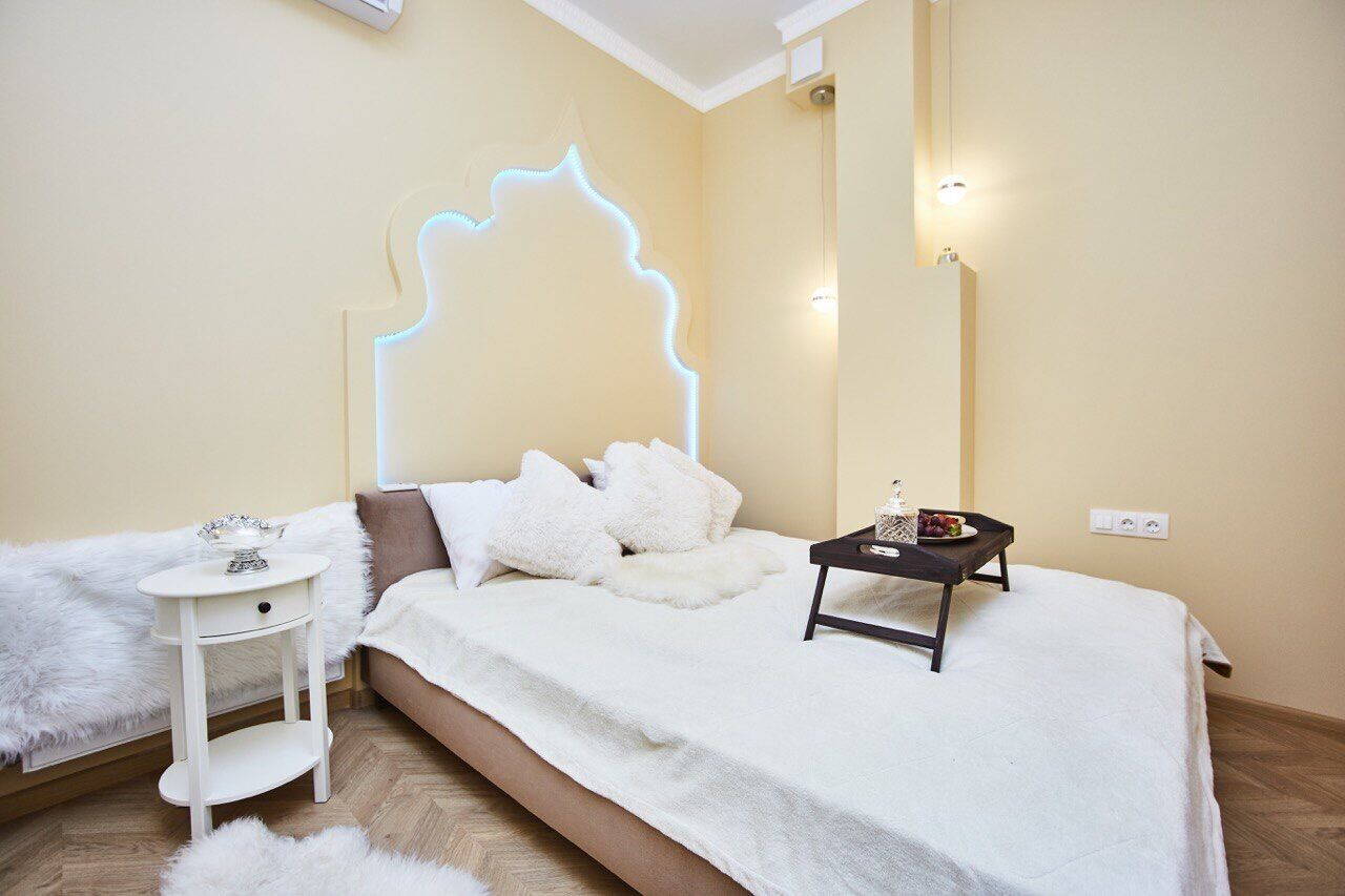 A bedroom with a bed, a small bedside table, a nightstand, and a wall-mounted light fixture.