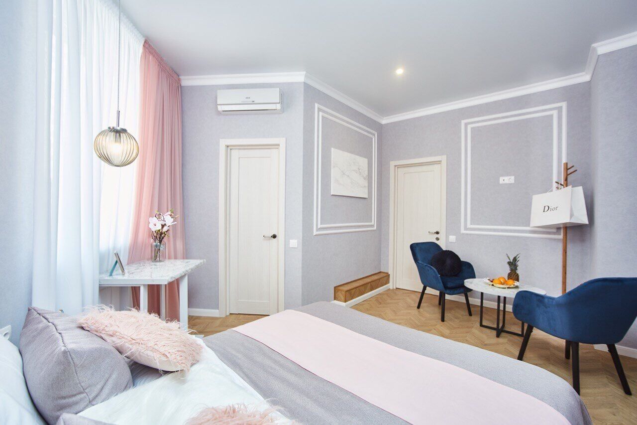 A modern bedroom with a bed, a desk, two chairs, and a small table with fruit.