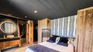 Un dormitorio moderno con una cama grande, un espejo redondo, un cabecero de madera y una escalera que lleva a un nivel superior.