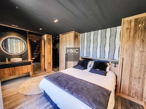 A modern bedroom with a large bed, a round mirror, a wooden headboard, and a staircase leading to an upper level. - Chalet "L'Oustal", superbe vue et Jacuzzi (Bolquère)