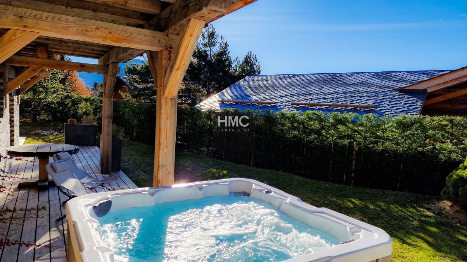 Ein Whirlpool unter einer hölzernen Pergola mit Blick auf ein Haus und einen eingezäunten Garten.