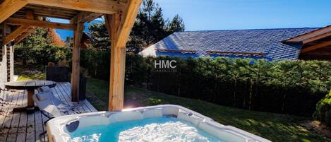 Ein Whirlpool unter einer hölzernen Pergola mit Blick auf ein Haus und einen eingezäunten Garten.