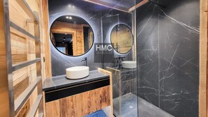 Un baño moderno con tocador de madera, dos espejos redondos y cabina de ducha con mampara de vidrio.