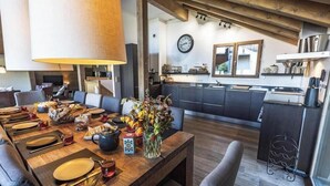 A dining area with a wooden table set for a meal, a kitchen with modern appliances, and a clock on the wall.