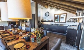 Zona pranzo con tavolo in legno apparecchiato per un pasto, cucina con elettrodomestici moderni e orologio a parete.