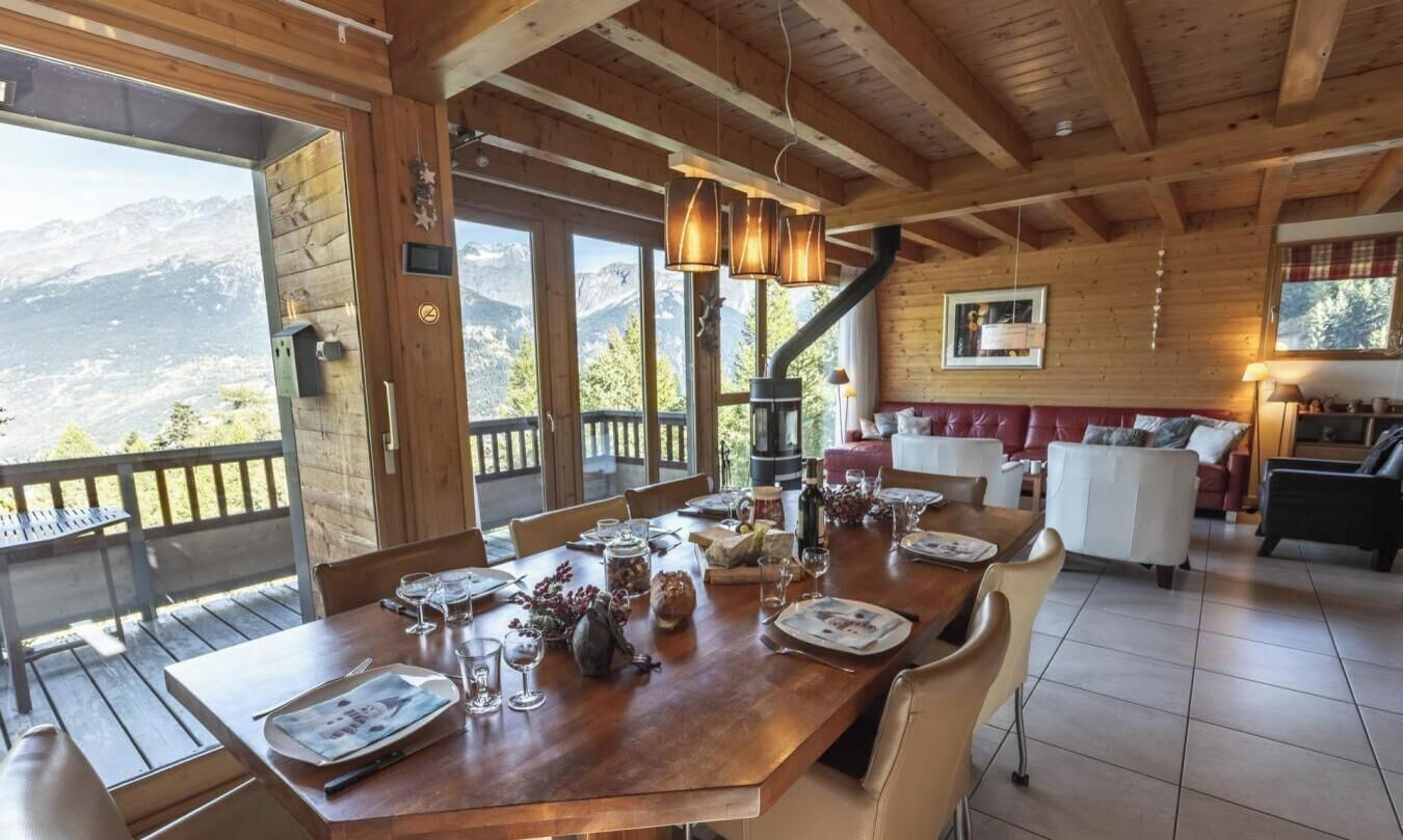 Ein Essbereich mit Holzboden, ein Tisch für vier Personen, große Fenster mit Blick auf die Berge und eine gemütliche Sitzecke mit Kamin.