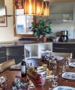 A dining table set with a bottle of wine, cheese, grapes, and a decorative mug.
