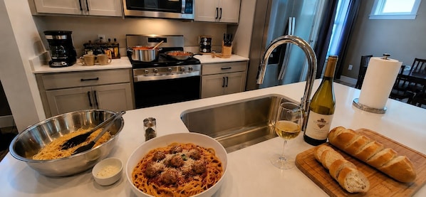 A kitchen with a stove, sink, and various cooking utensils. There is a bowl of spaghetti, a bottle of wine, and a loaf of bread on the counter. - Mocha Haven King Bed Quiet Walkable To Parks, Coffee, Yellowstone River (Billings)
