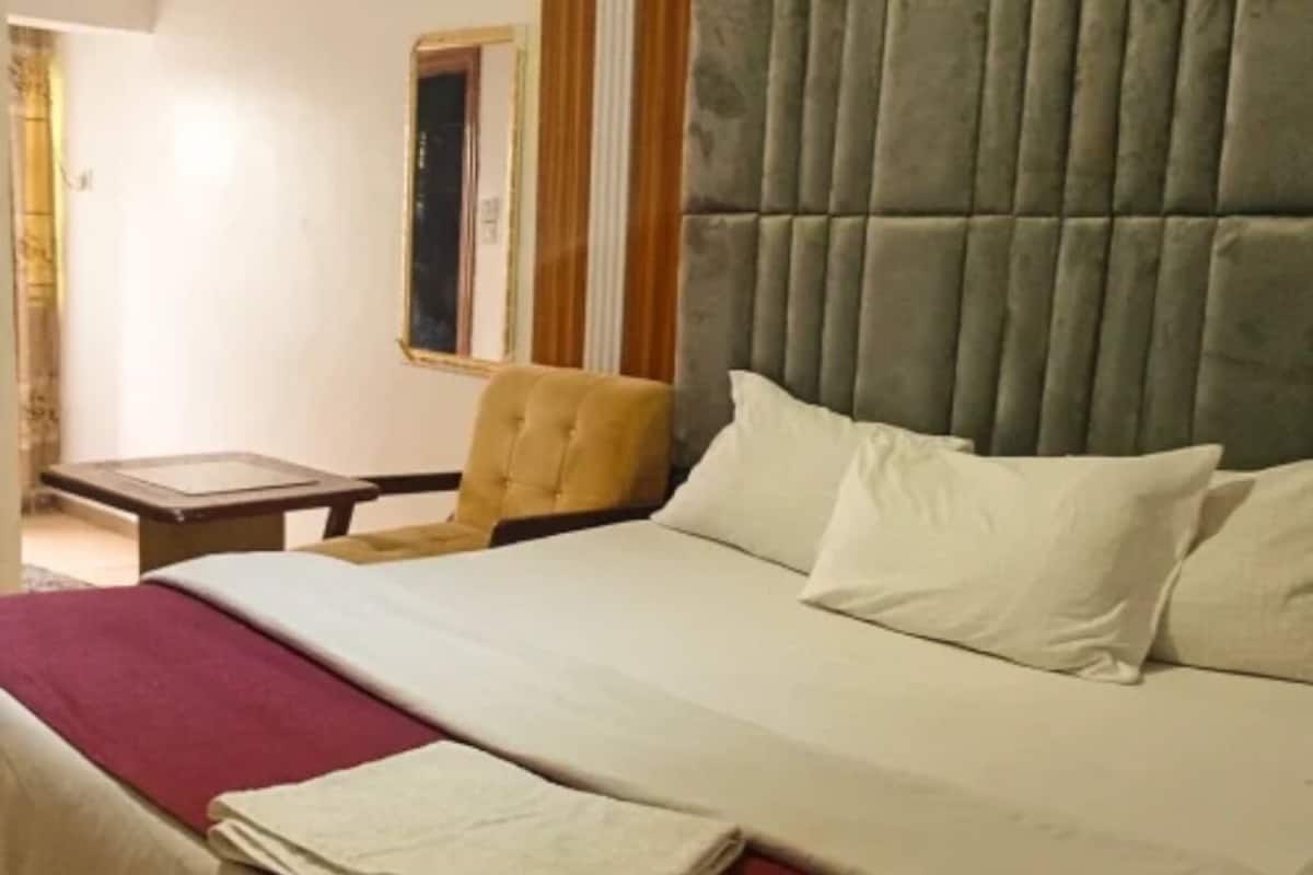 Ein Hotelzimmer mit einem Bett, einem Sessel, einem kleinen Tisch und einem Fenster mit Vorhängen.