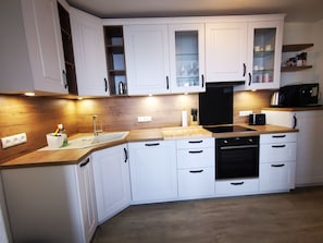 Eine moderne Küche mit weißen Schränken, einer Holzarbeitsplatte, einer Spüle, einem Geschirrspüler und einem schwarzen Backofen.
