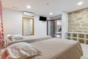 A bedroom with two beds, a TV, and a stone wall.