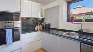 A modern kitchen with white cabinets, a stainless steel oven, a sink, and a window with a view of the outdoors.