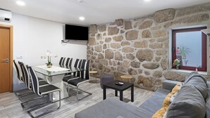 A modern living room with a stone wall, a flat-screen TV, a sofa, and a dining area with chairs and a table.