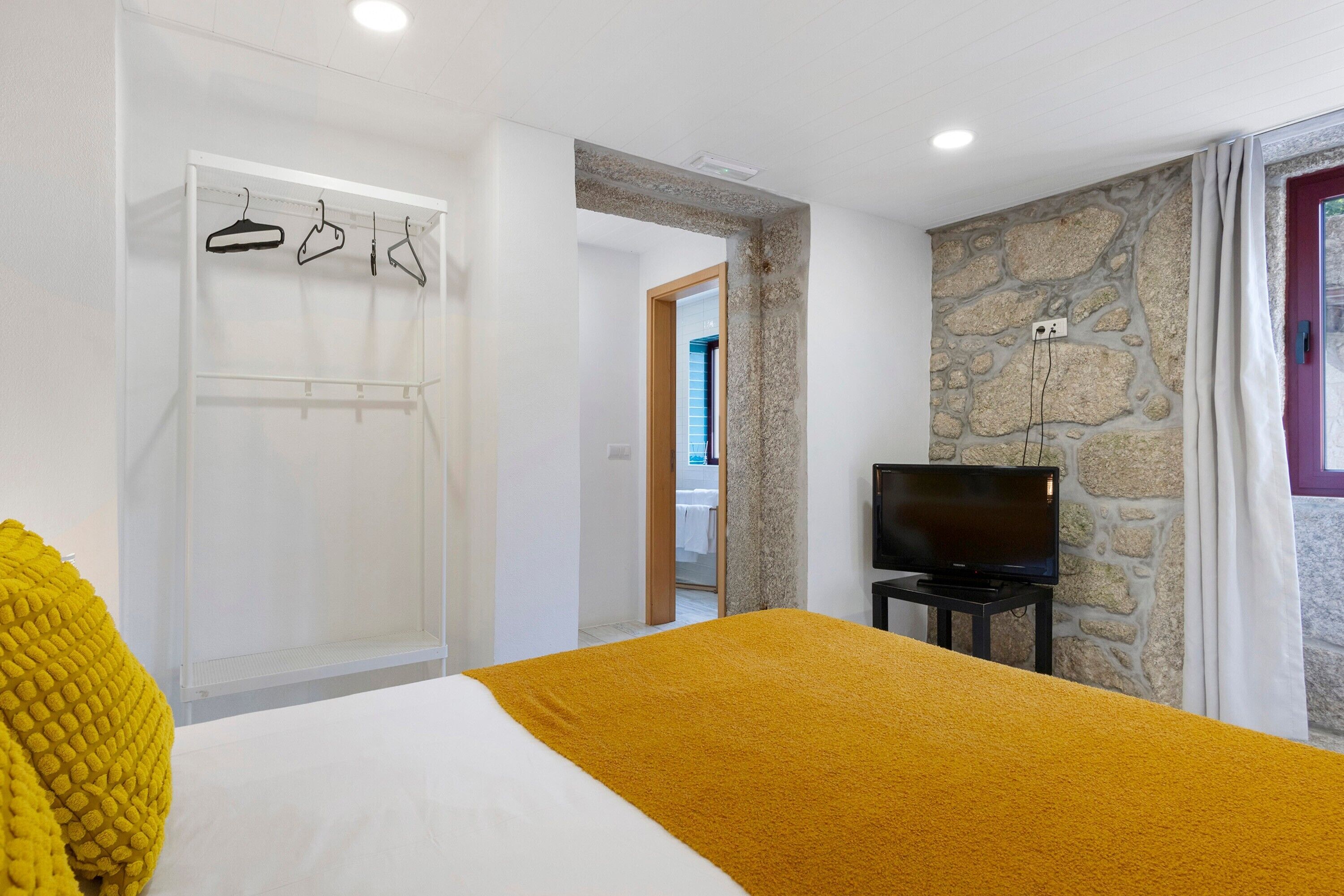 Un dormitorio con una cama, televisor, armario y pared de piedra.