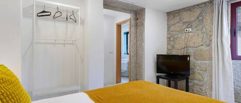 Un dormitorio con una cama, televisor, armario y pared de piedra.