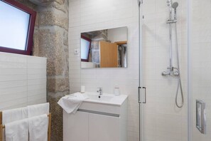 A bathroom with a stone wall, a mirror, a sink, a shower, and a window.
