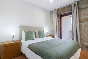 Ein Schlafzimmer mit einem Bett, zwei Nachttischen, einem Fenster mit Vorhängen und einer Steinwand.
