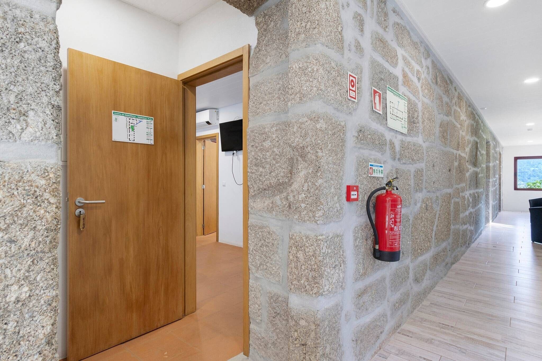 A hallway with a stone wall, a wooden door, a fire extinguisher, and a sign on the wall.