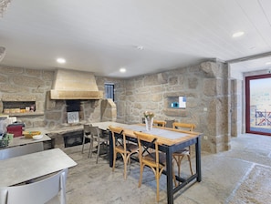 Une pièce aux murs de pierre, dotée d’un four encastré, d’une table avec des chaises et offrant une vue à travers une porte.