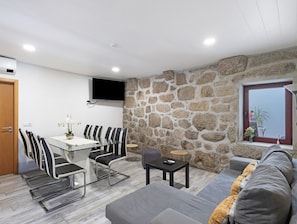 Una sala moderna con pared de piedra, televisor de pantalla plana, sofá y comedor con sillas y mesa.