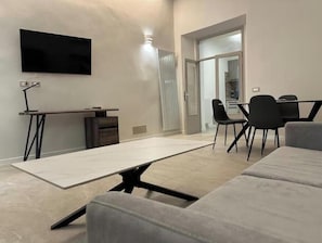 A modern living room with a sofa, a coffee table, a TV mounted on the wall, and a dining area with chairs and a table. - Residenza Aurea Tivoli - Historical Elegance in the Heart of Tivoli (Tivoli)