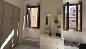A bedroom with a large wardrobe, a bedside table, a mirror, and a window with an open shutter.