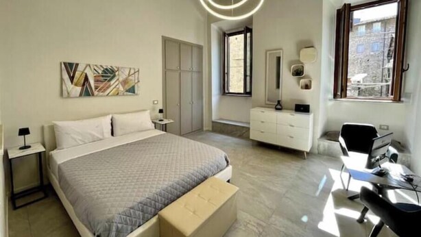 A modern bedroom with a bed, bedside tables, a dresser, a desk, and a large window.