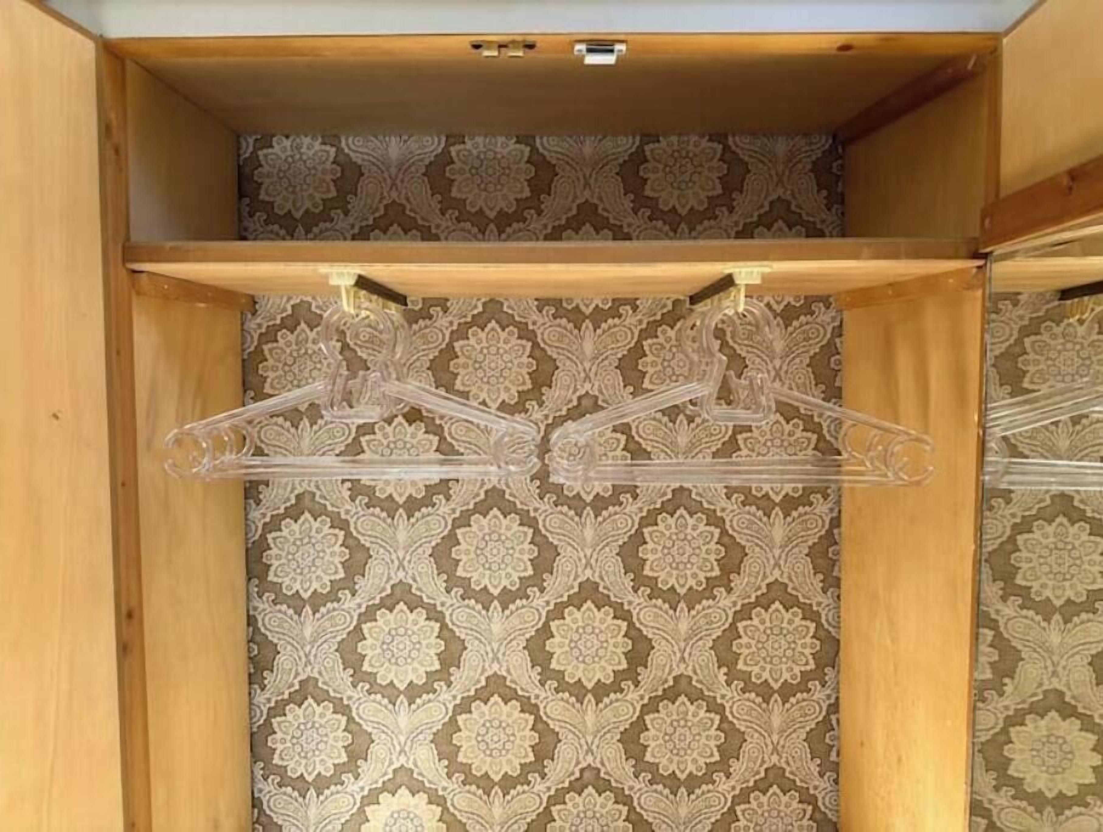 A wooden closet with patterned wallpaper, two empty plastic hangers, and a wooden shelf.